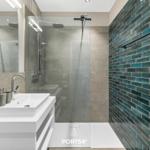 Badezimmer mit Dusche, Waschbecken und blauen Fliesen an der Wand.