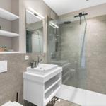 Badezimmer mit Dusche, Waschbecken und Regalen. Wandfliesen und Spiegel sichtbar.