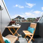 Terrasse mit Tisch und zwei Stühlen, Blick auf Haus und Himmel.
