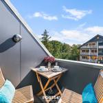 Terrasse mit Tisch und zwei Stühlen, Blick auf ein Gebäude und Bäume.