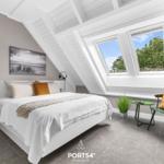 Schlafzimmer mit Dachfenster, Bett, Nachttisch und Sitzgelegenheit.