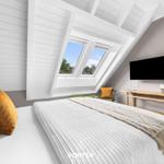 Schlafzimmer mit Dachfenster, Bett, TV und Holztisch.