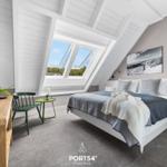 Schlafzimmer mit Dachschrägen, Doppelfenster und Bett mit grauer Bettwäsche.