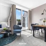 Wohn- und Essbereich mit Sofa, Stühlen und Tisch. Große Fenster mit Blick nach draußen.