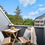 Terrasse mit Tisch, zwei Stühlen, Kissen und Obst. Blick auf grüne Bäume und ein Haus.