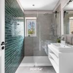 Badezimmer mit Dusche, Waschbecken und grüner Fliesenwand. Fenster mit Blick auf Außenbereich.