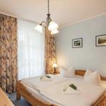 Schlafzimmer mit Holzbett, Fenster und Nachttischen.