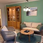Wohnzimmer mit Sofa, Sessel und Holzregal an grüner Wand.