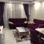 Wohnzimmer mit lila Sofa, Tisch und Teppich auf Marmorfliesen.