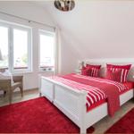 Schlafzimmer mit weißem Bett, rotem Teppich und Fenstern mit Blick nach draußen.