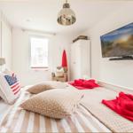 Schlafzimmer mit Bett, TV und Fenster. Rote Decke und Kissen mit US-Flagge.