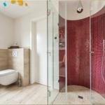 Bad mit Dusche und Toilette. Duschbereich mit roten Mosaikfliesen.