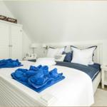 Schlafzimmer mit weißem Bett, blauen Handtüchern und Schrank unter Dachschräge.