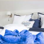 Schlafzimmer mit Bett, Kissen und Nachttisch mit Lampe.