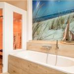 Bad mit Badewanne und Sauna. Wandbild zeigt Strand mit Segelboot.