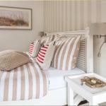 Ein Bett mit Streifenbezug und Kissen, daneben Nachttisch und Wandlampe.