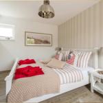 Schlafzimmer mit Bett, Nachttisch und Wandbild. An der Wand hängt ein Fernseher.