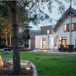 Modernes Haus mit Terrasse, Garten und Grillplatz bei Abenddämmerung.