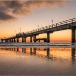 Eine Pier mit Laternen und einem Leuchtturm am Strand bei Sonnenuntergang.