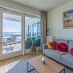 Wohnzimmer mit Sofa, Couchtisch und Balkonblick auf das Meer.