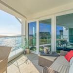 Terrasse mit Meerblick, Wickermöbel und Glasgeländer. Durchgang in Wohnbereich.