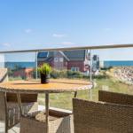 Terrasse mit Tisch und Stühlen, Blick auf Meer und rotes Haus.
