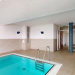 Innenpool mit Metalltreppe und hellen Wänden. Türen und Säulen sind sichtbar.