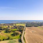 Ausblick auf Küstenlandschaft mit Feldern, Wald und Hafen.