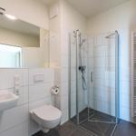 Badezimmer mit Dusche, Waschbecken und WC. Fliesen und Spiegel sind vorhanden.