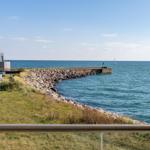 Meerblick mit Steinhafen und rotem Haus am Strand.