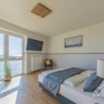 Schlafzimmer mit Blick aufs Meer, Bett, Fernseher und Wandbild mit Segelbooten.