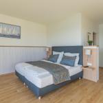 Schlafzimmer mit Doppelbett, Wandbild und Holzboden. Nebenraum sichtbar.