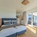 Schlafzimmer mit Doppelbett, Balkon und Holzboden.