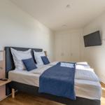 Schlafzimmer mit Doppelbett, Kleiderschrank und Wandfernseher. Fenster mit Pflanze.