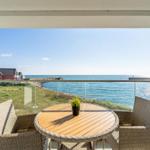 Terrasse mit Tisch und Stühlen bietet Blick auf Meer und Strandhaus.