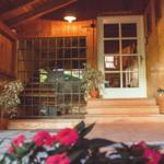 Eingangsbereich mit Holzwand, Glasfenster und Pflanzen. Tür führt ins Innere.