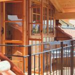 Terrasse mit Holzgeländer und Sitzbank unter Dach, Blick auf Dachziegel und Berge.