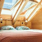 Doppelbett unter Dachschrägen mit Dachfenstern und Holzwänden.