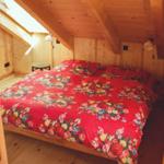Schlafzimmer mit Holzwand, Dachboden und Bett mit blumigem Bettbezug.