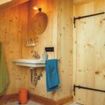 Badezimmer mit Holzwand, Waschbecken, Dusche und Handtüchern.