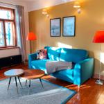 Ein Wohnzimmer mit blauem Sofa, zwei orangefarbenen Stehlampen und einem Fenster mit Blick nach draußen.