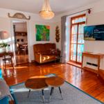 Wohnzimmer mit Holzboden, Sofa, Fernseher und Blick auf Balkon.