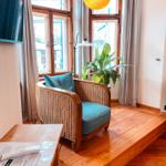 Ein Sessel mit blauem Kissen steht auf einer Holzplattform vor Fenstern mit Vorhängen.