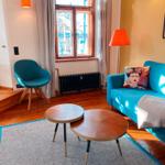 Ein Wohnzimmer mit blauem Sofa, Stuhl und zwei runden Tischen auf Teppich.