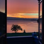 Von der Terrasse aus bietet sich ein Blick auf einen See bei Sonnenuntergang mit einem einzelnen Baum.