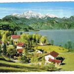 Haus mit rotem Dach am See, umgeben von Wäldern und Bergen mit Schnee.