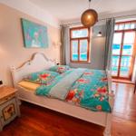 Schlafzimmer mit Bett, Fenster und Holzboden. An der Wand hängt ein Gemälde.