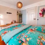 Schlafzimmer mit Bett, Wandbild und Holzboden. Decke mit floraler Bettwäsche.