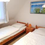 Two single beds with wooden frames and white bedding. Between them stands a nightstand with a lamp.