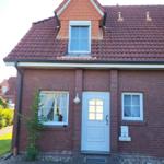 Red tiled roof, white door and windows. House with paved front garden.